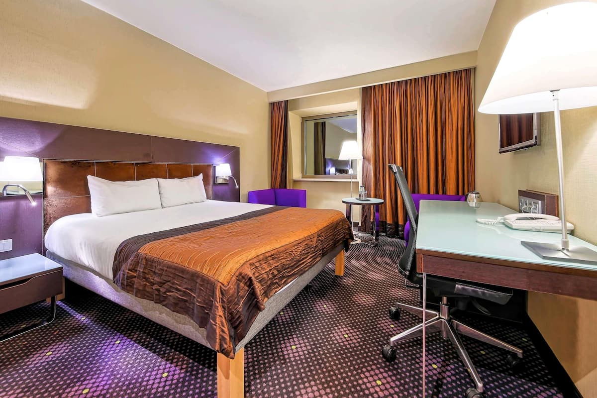Une chambre d’hôtel comprenant un lit, un bureau, une chaise, une petite table, une lampe, un téléphone et un miroir.