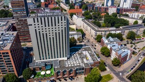 Un edificio alto con fachada de diseño enrejado, rodeado de otros edificios y vegetación.