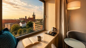 Une chambre d’hôtel avec vue sur la ville, un coin fenêtre avec un livre, une tasse de café, une bouilloire et une lampe.