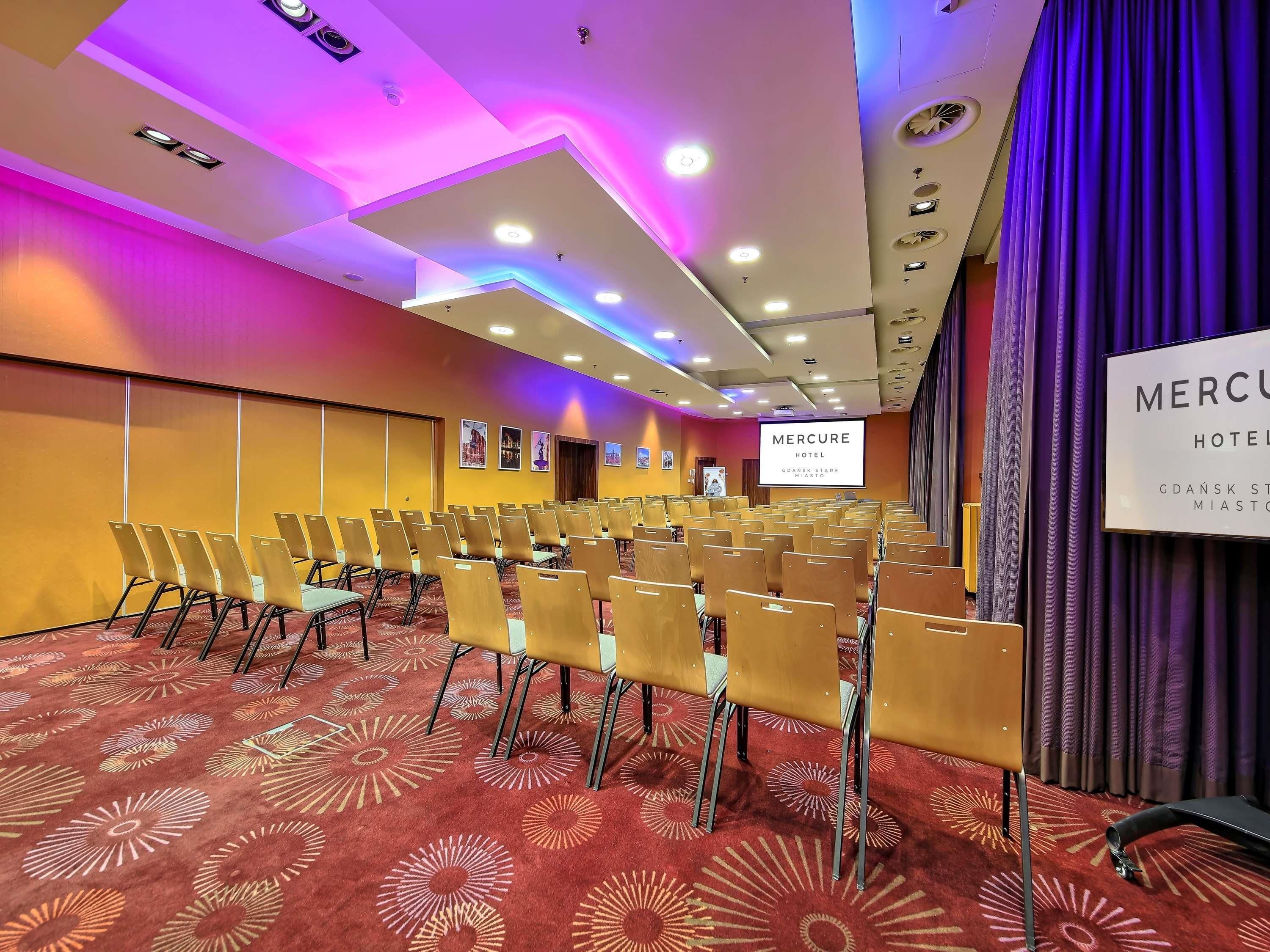 A conference room with rows of chairs, a projection screen, and a sign indicating it's part of the Mercure Hotel.