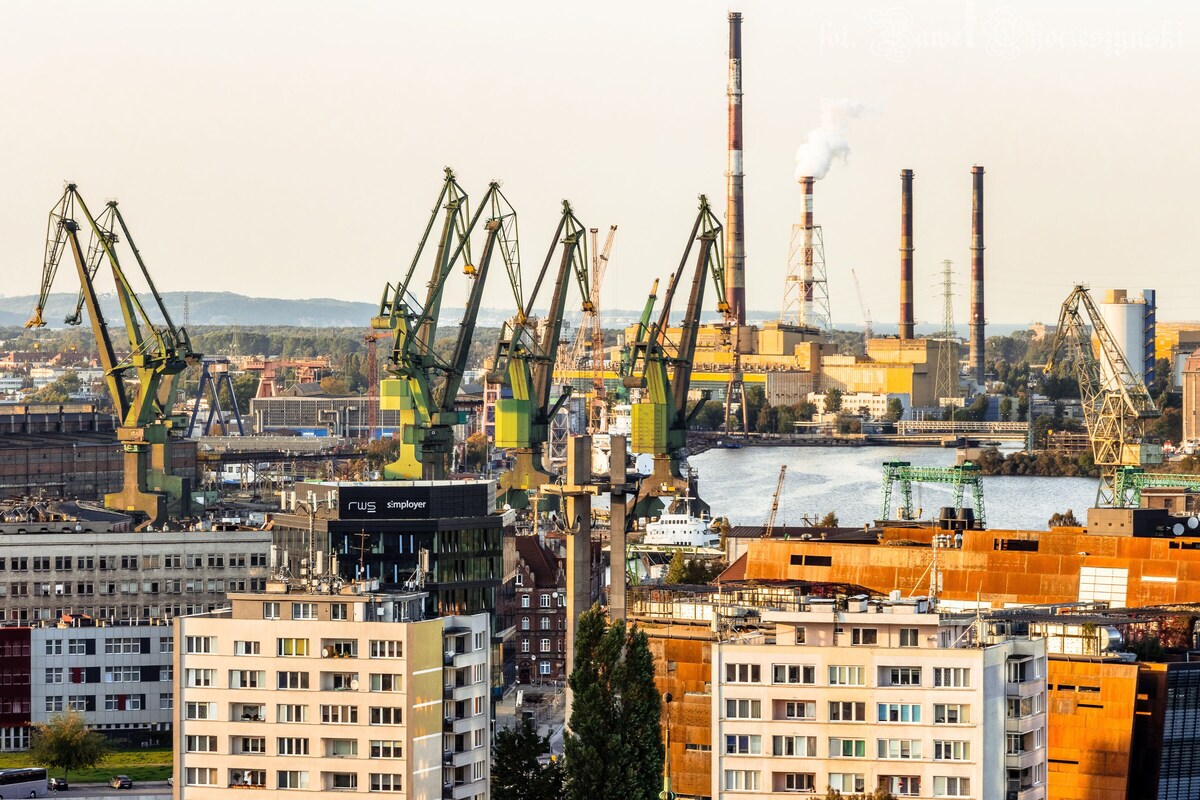 A cityscape with industrial cranes, a river, and buildings.