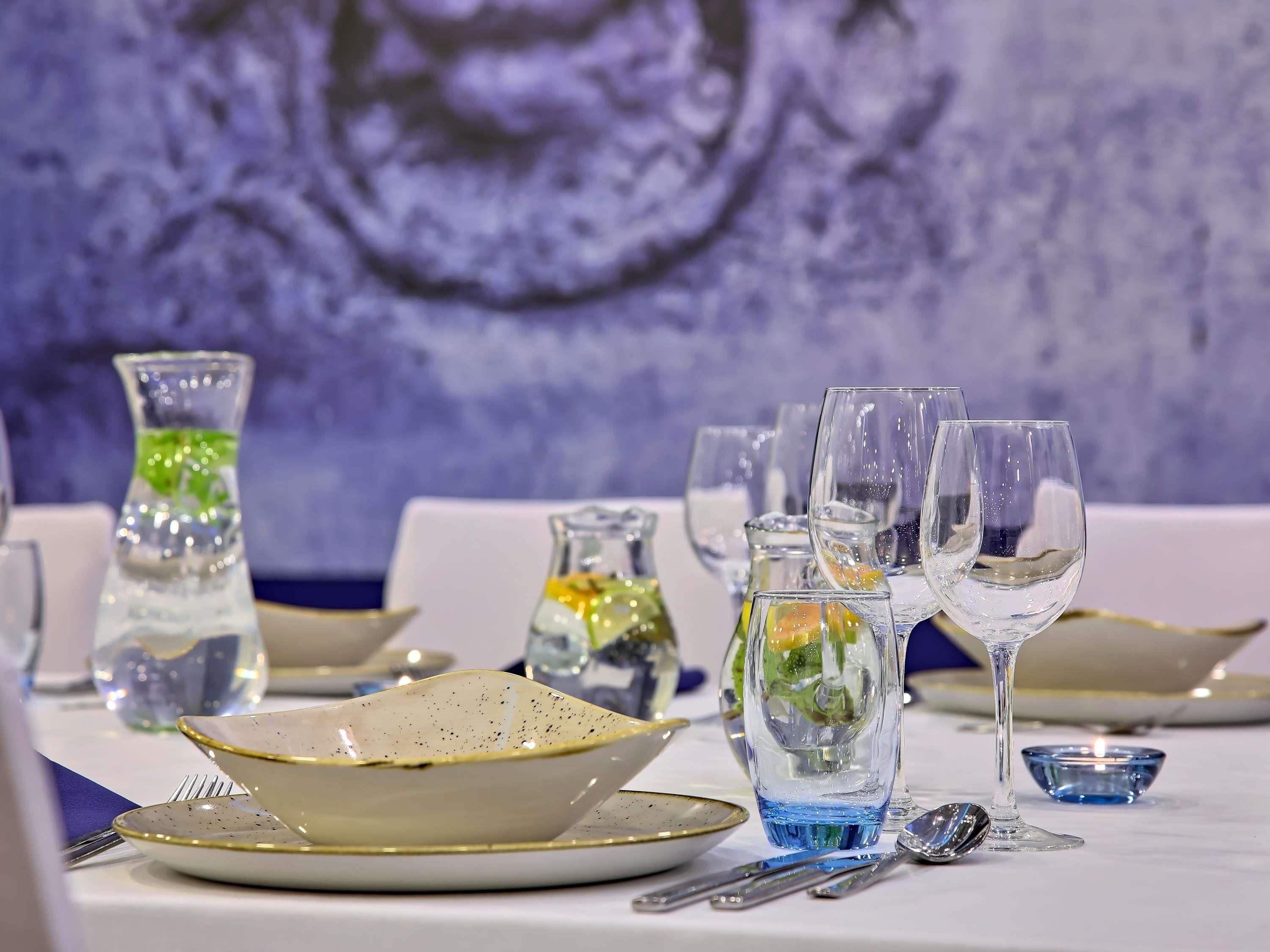 Una mesa dispuesta con vasos transparentes, platos y una jarrón, presumiblemente para una comida.