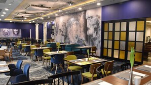 Un restaurant moderne offrant différents types de sièges, notamment des tables et des banquettes, un tapis à motifs et une grande fresque murale.