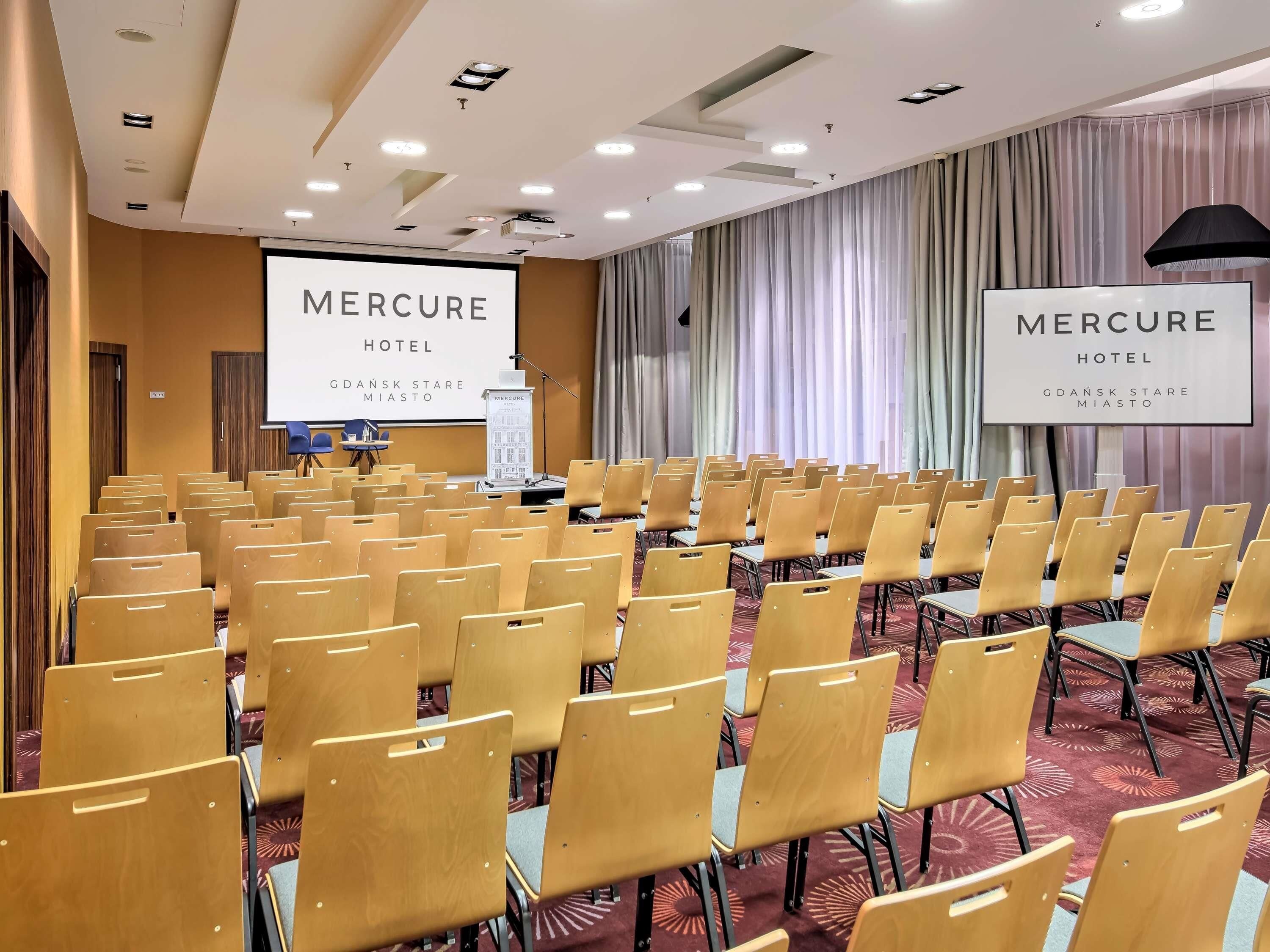 A conference room at Mercure Hotel with rows of chairs, a podium, and a projection screen.