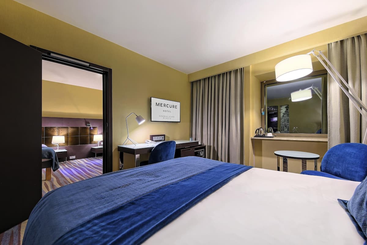 A hotel room with a bed, desk, chair, lamp, and a sign that reads 'Mercure Hotel.'