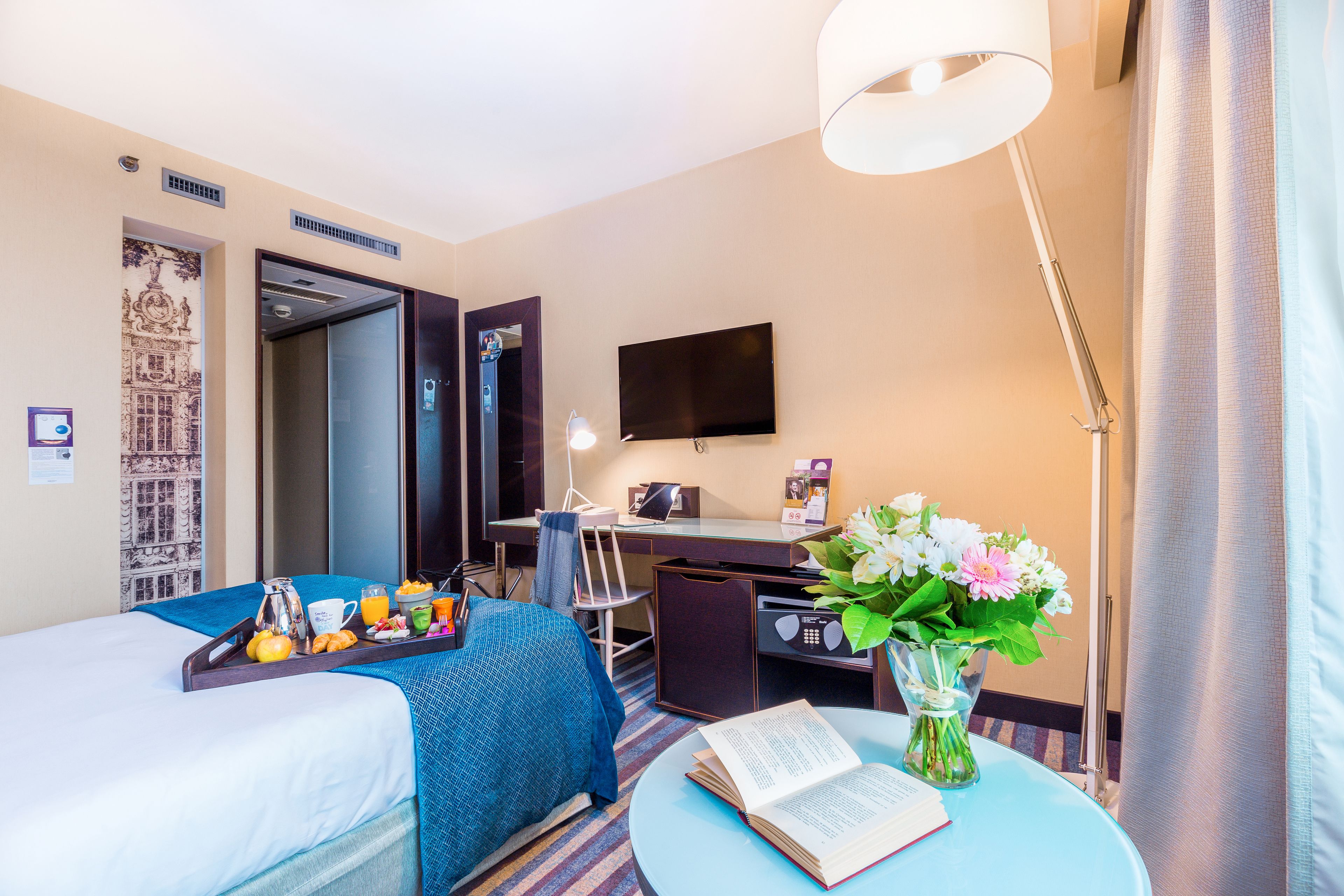 Habitación de hotel con dos camas, un escritorio, un televisor, una lámpara y un florero con flores.