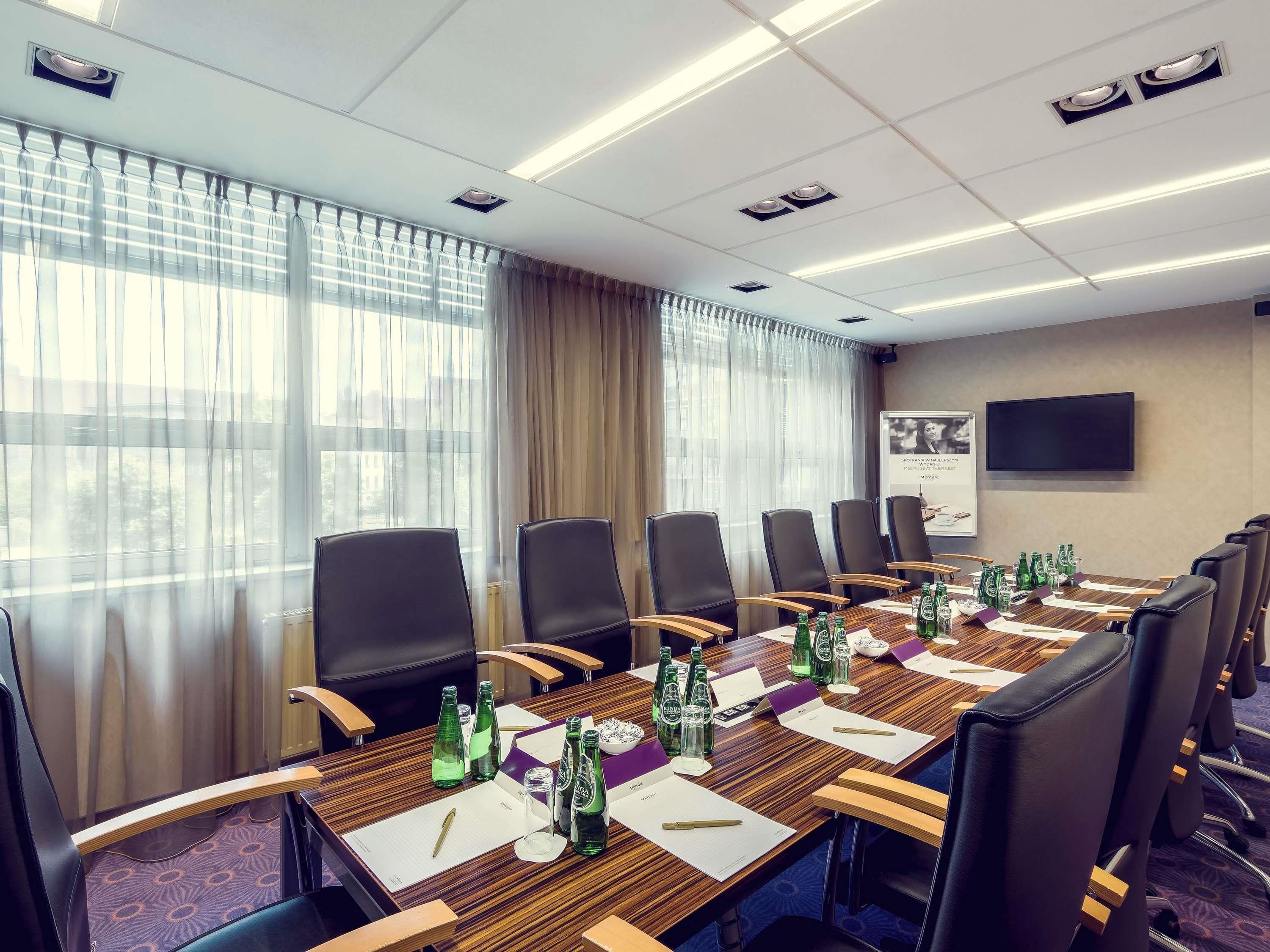 Un salón de conferencias con una mesa larga, sillas y un televisor en la pared.