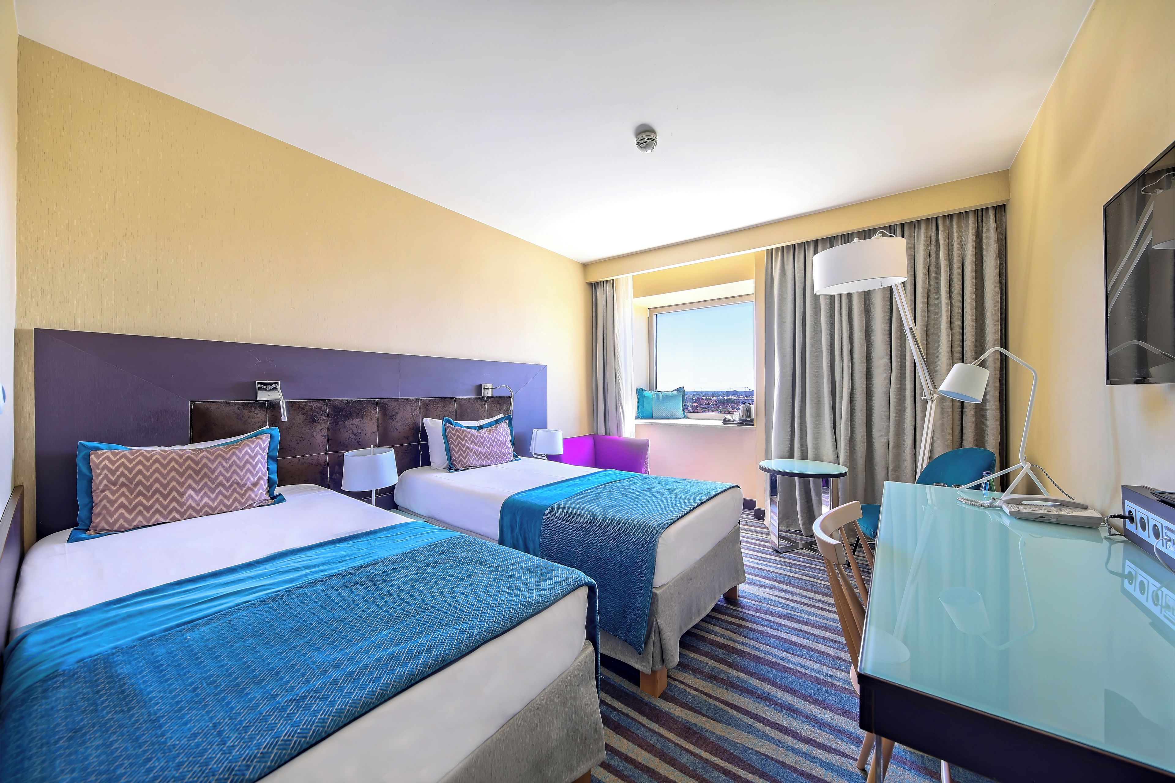 Une chambre d’hôtel avec deux lits, un bureau, une chaise, une télévision et une fenêtre donnant sur un beau paysage.