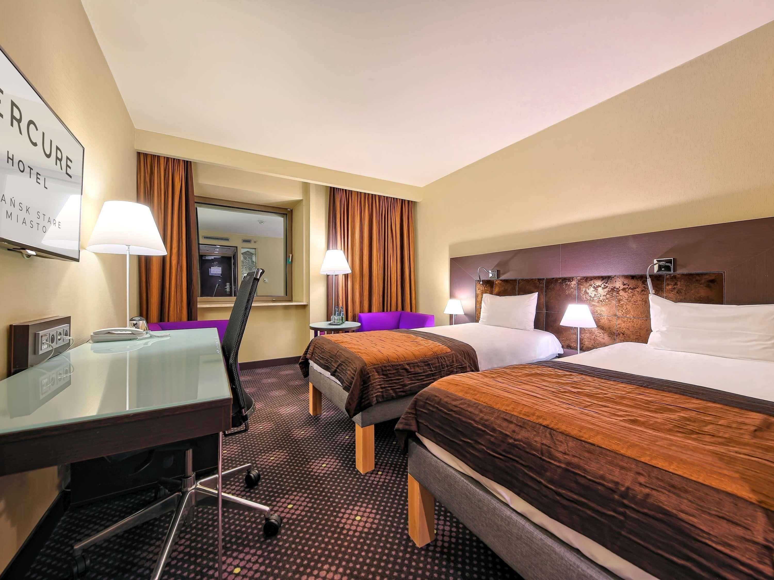 A hotel room with two beds, a desk, a chair, a small table, and a mirror.