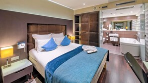 Una habitación de hotel moderna con una cama grande, mesitas de noche, un baño con bañera y un espejo.