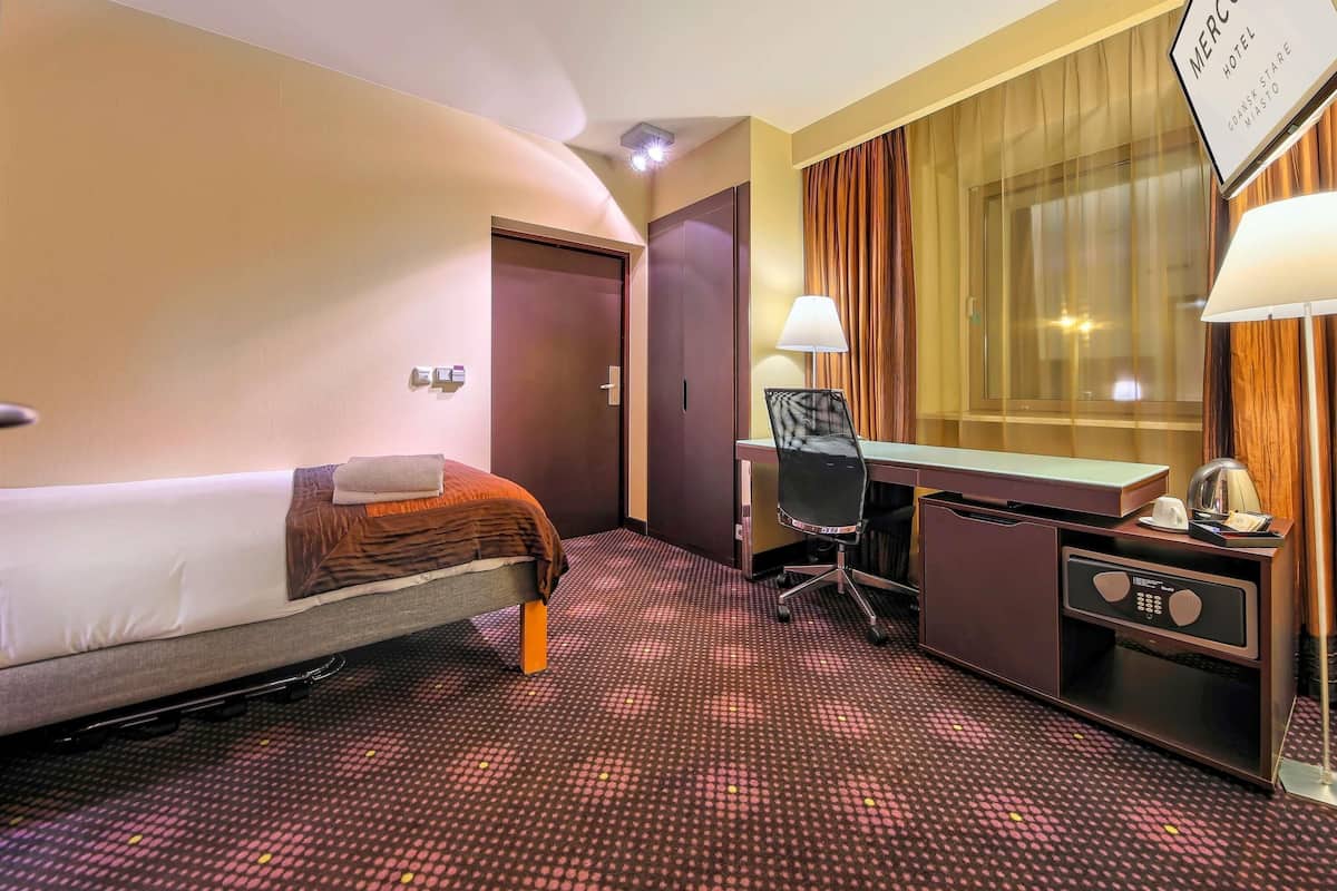 Una habitación de hotel con cama, escritorio, silla y un cartel con el nombre del hotel.