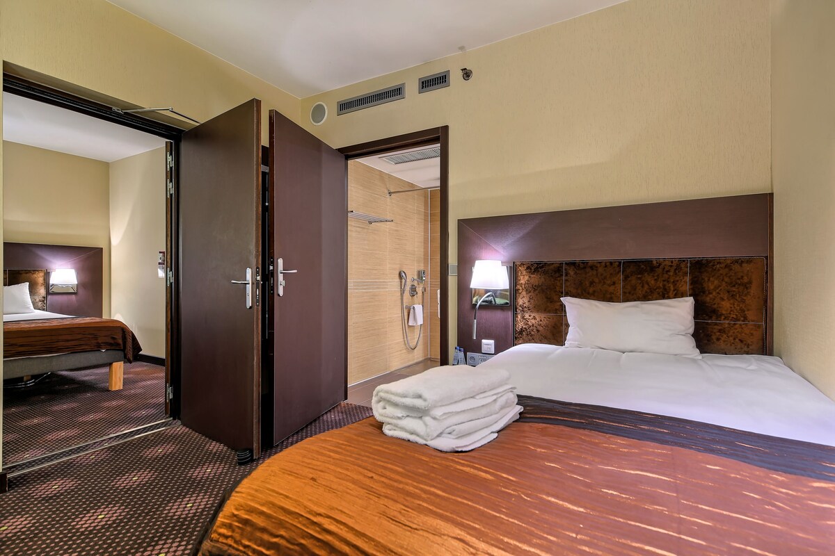 A hotel room with a bed, a bathroom, and a door to another room.