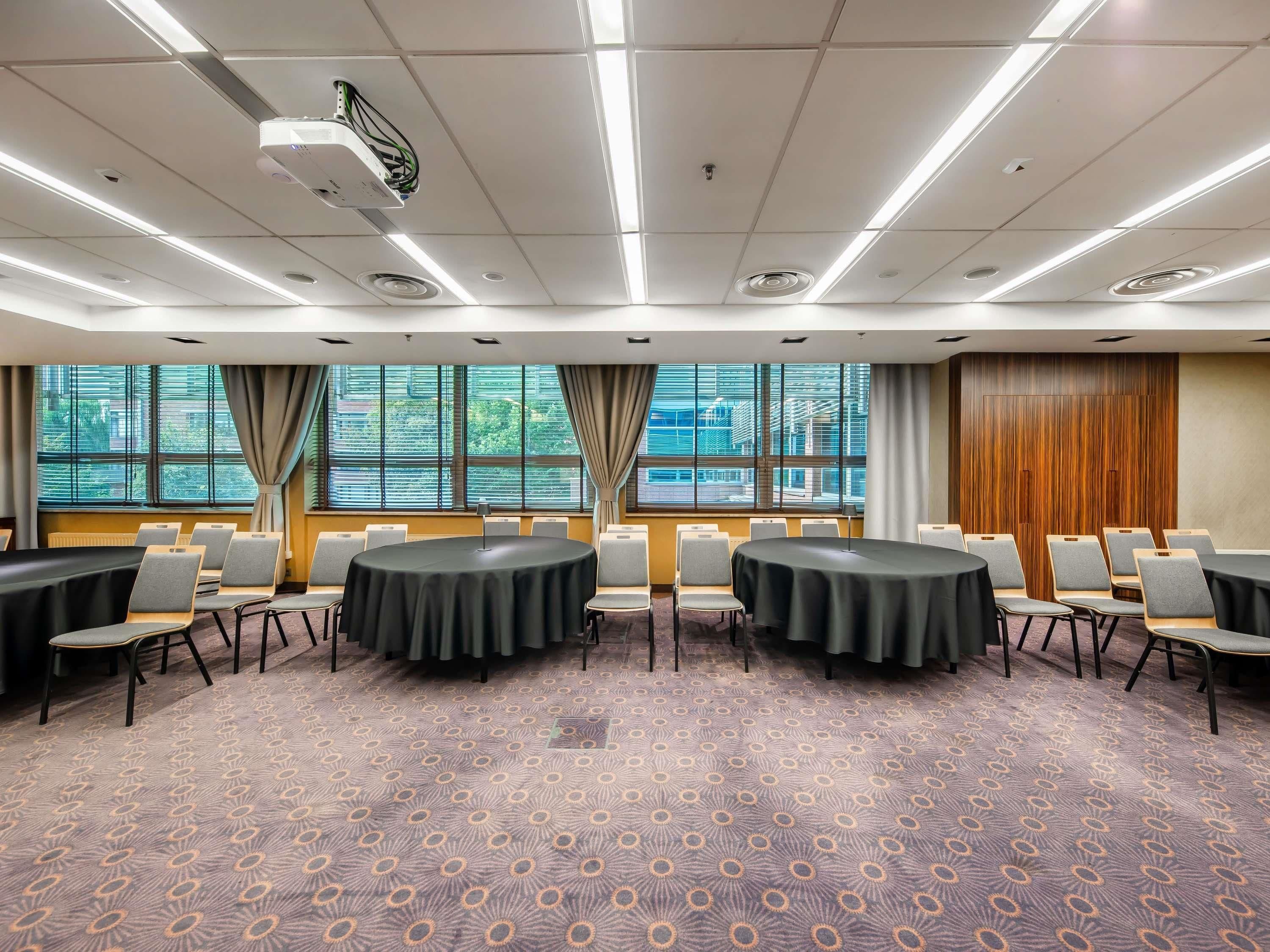 A conference room with round tables, chairs, and a patterned carpet.