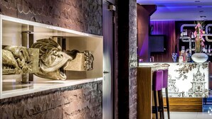 Un interior moderno con una pared de piedra, una zona de bar con mostrador y taburetes, y una escultura decorativa en exhibición.