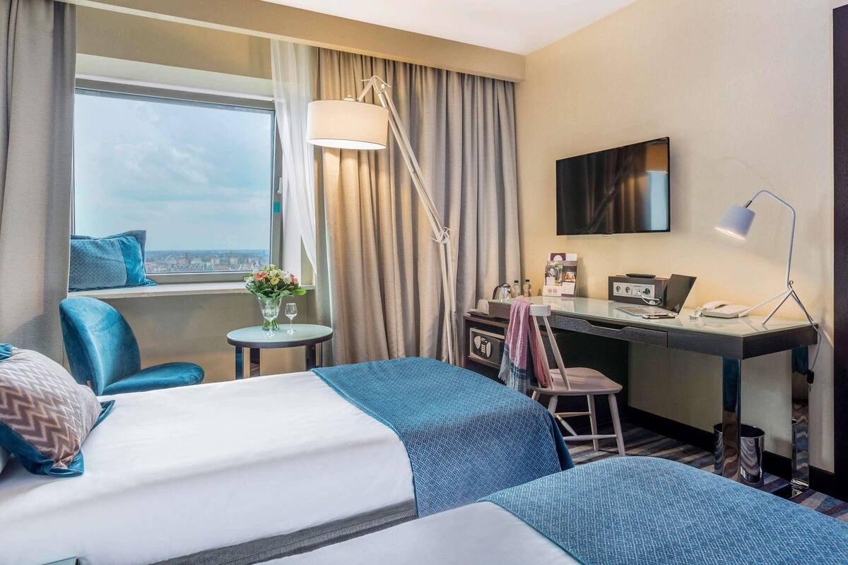 Habitación de hotel con dos camas, un escritorio, una silla, un televisor y una ventana con vistas.