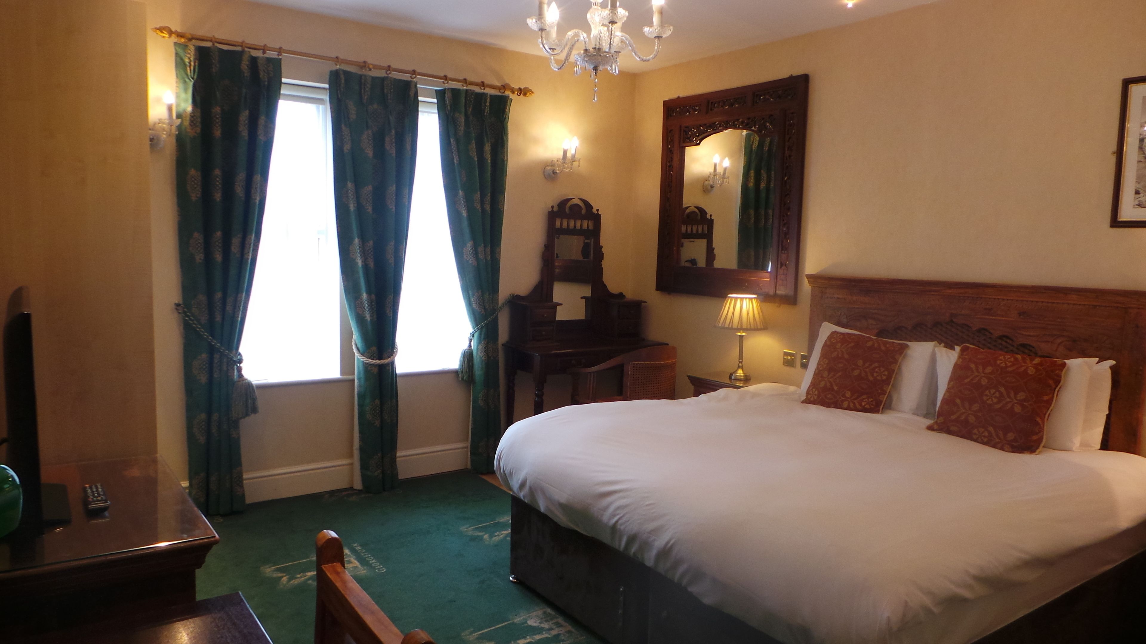 A bedroom with a large bed, a wooden dresser, a mirror, and a chandelier.