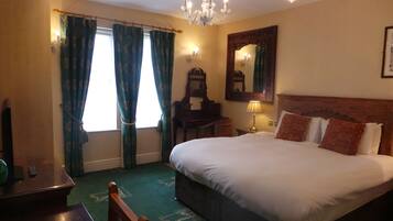 A bedroom with a large bed, a wooden dresser, a mirror, and a chandelier.