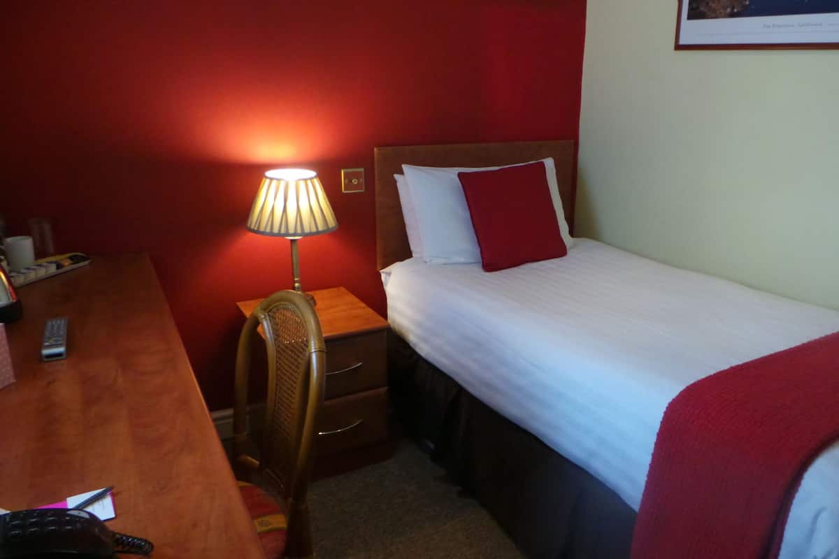 A hotel room with a bed, a nightstand, a lamp, a chair, and a desk.