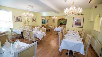 A dining area with multiple tables set for service, chandeliers, and framed artwork on the walls.
