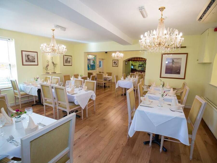 A dining area with multiple tables set for service, chandeliers, and framed artwork on the walls.