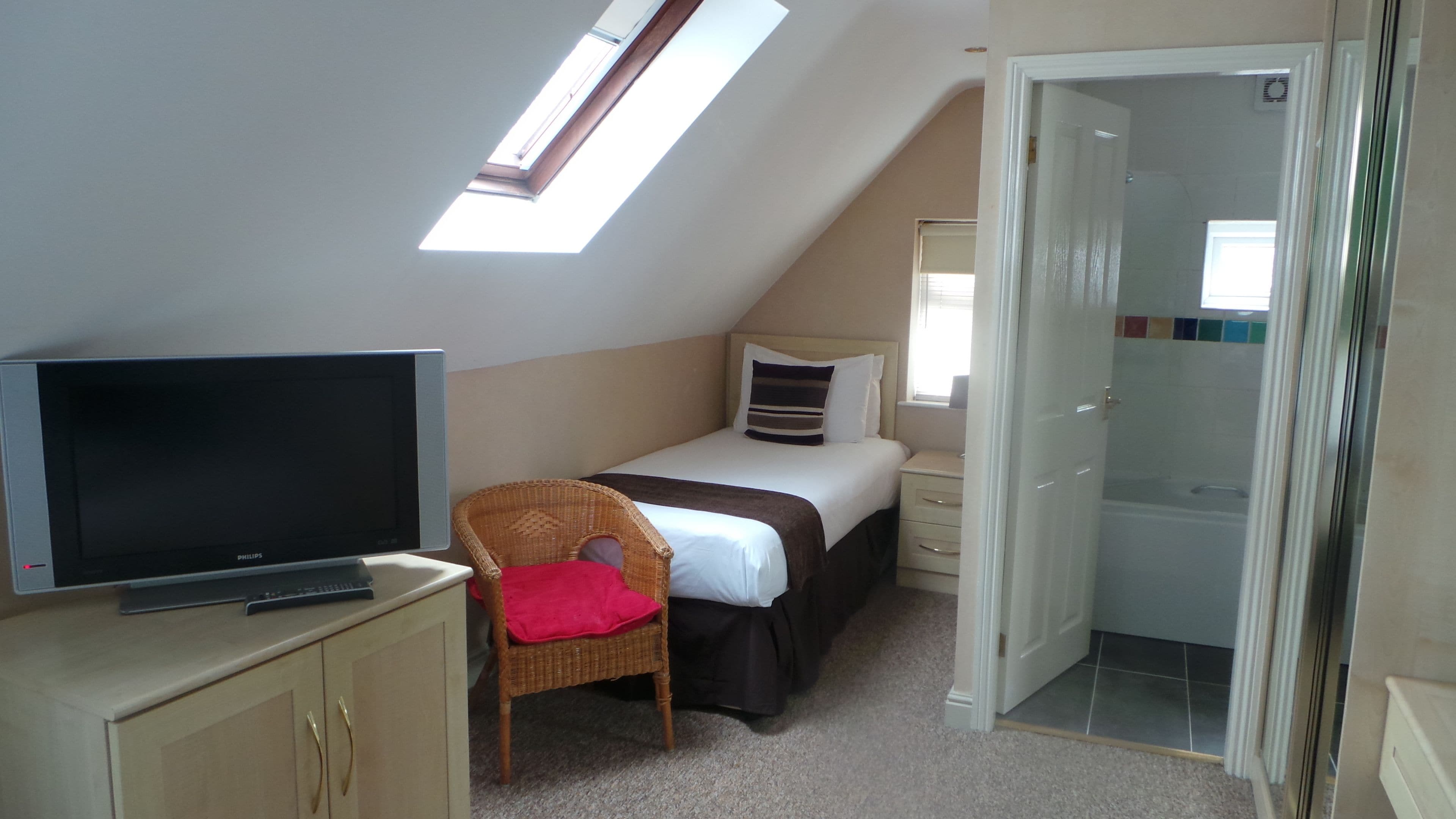 A bedroom with a bed, a television, a wicker chair, a small table, and a bathroom door.