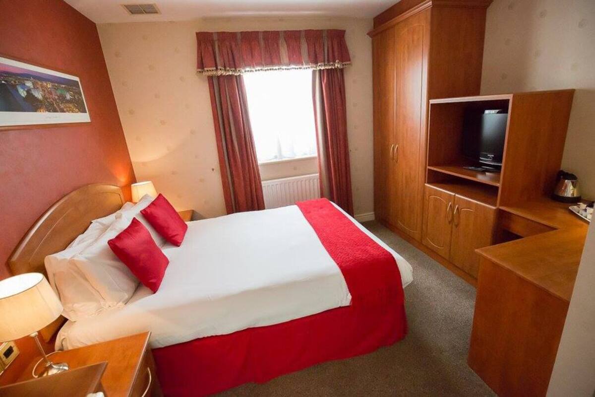 A hotel room with a bed, a television, a cabinet, and a window with curtains.