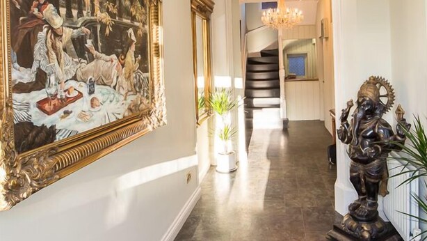 Un couloir orné d’un grand tableau, d’une statue et d’un escalier menant à un deuxième étage.