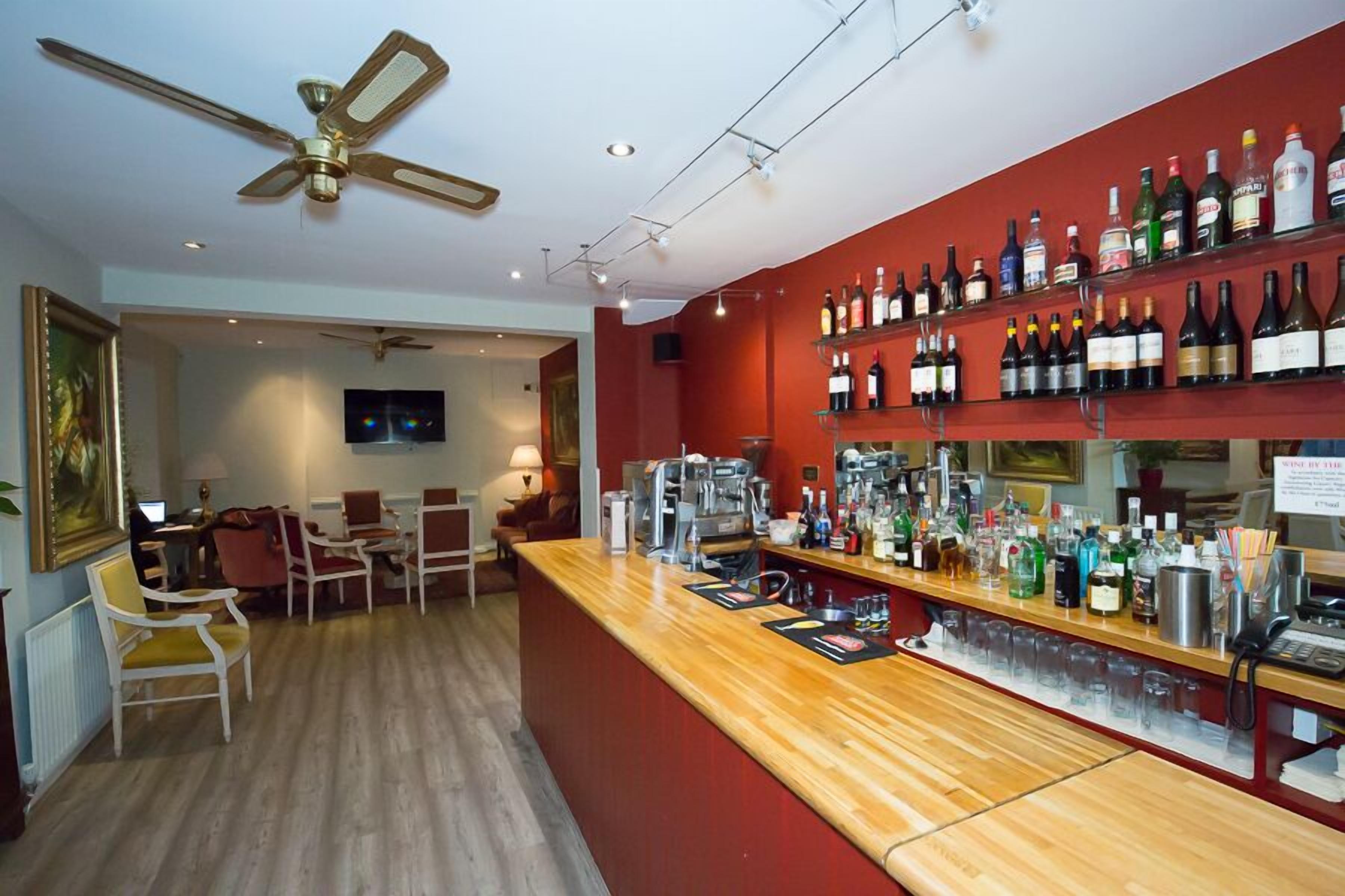 A bar area with a wooden counter, shelves of various liquor bottles, and a ceiling fan.