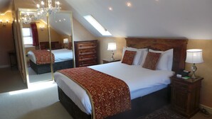 Une chambre avec un grand lit, un miroir, un lustre et une lucarne.