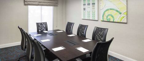 A conference room with a dark wooden table, black chairs, a patterned carpet, and two abstract paintings on the wall.