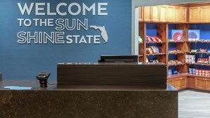 A reception desk with a "Welcome to the Sun Shine State" sign, a payment terminal, and a snack bar with various food items. - Hampton Inn & Suites by Hilton Miami-Doral/Dolphin Mall (Miami)