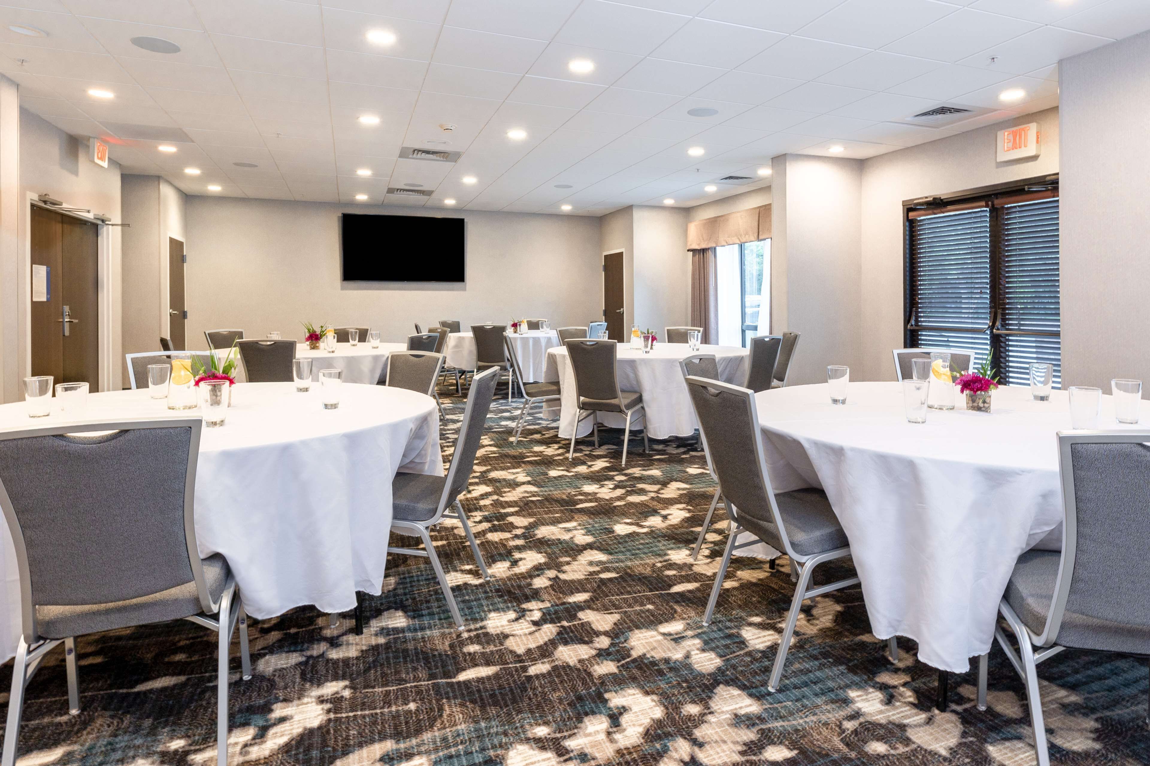 A conference room with round tables, chairs, and a carpeted floor.