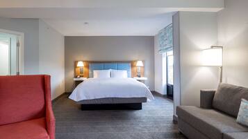 Una habitación de hotel con una cama grande, dos mesitas de noche con lámparas, un sillón rojo y un sofá gris.