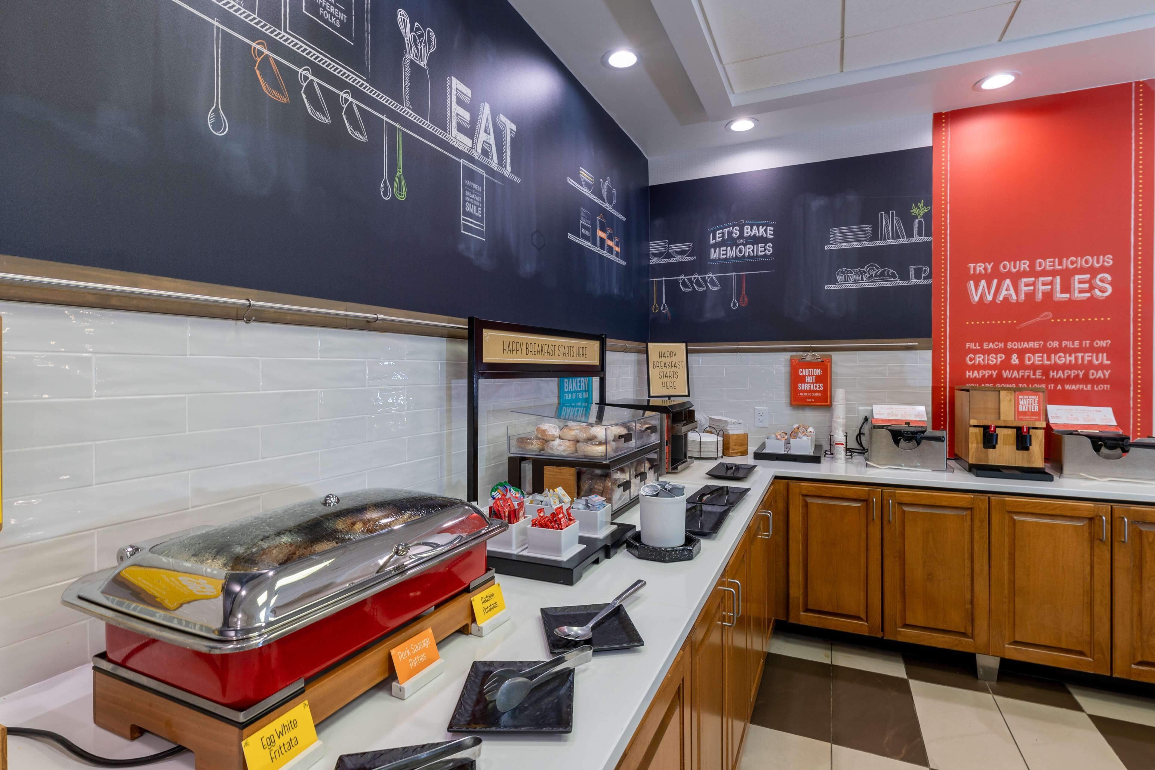 A breakfast buffet area with a variety of food items, including a hot food station, and a sign promoting waffles.