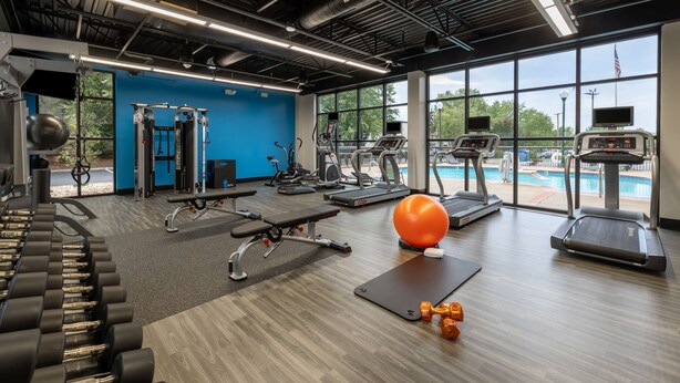 A gym with various exercise equipment, a large window with a view of a swimming pool, and a blue accent wall. - Hampton Inn Christiansburg/Blacksburg (Christiansburg)