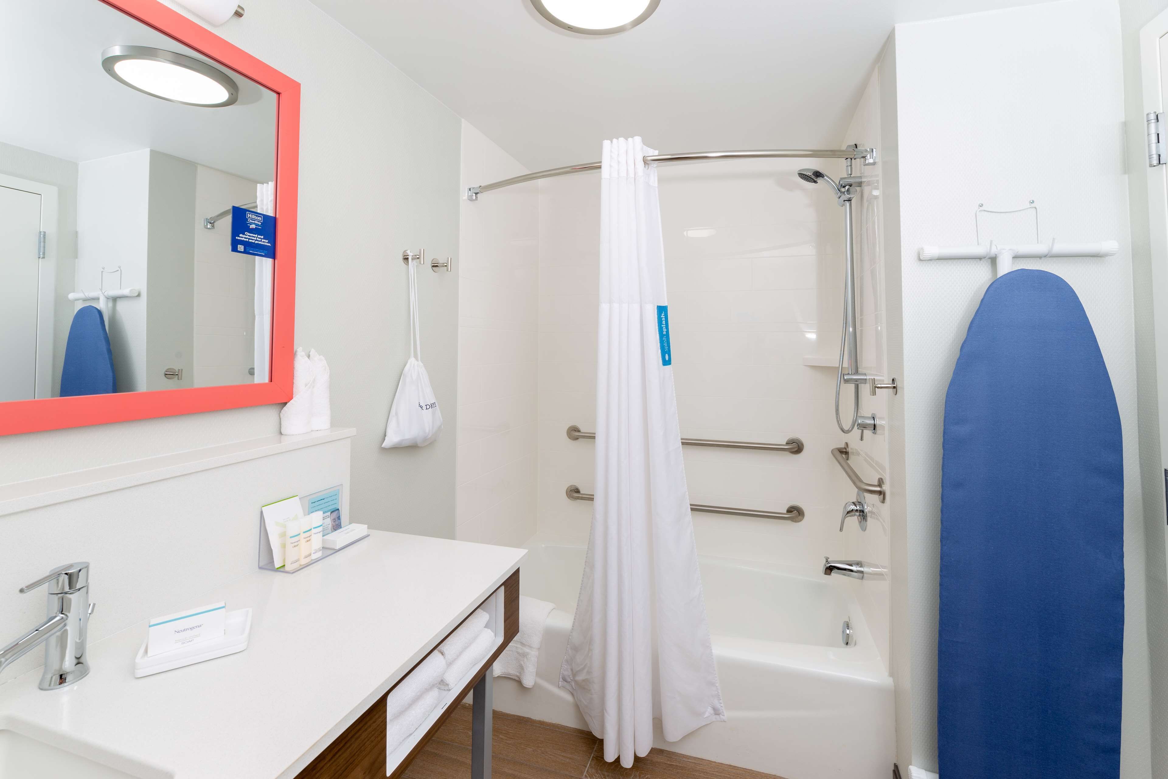 Een moderne badkamer met een witte wastafel, een spiegel met rode omlijsting, een douche met een witte douchegordijn en een blauwe handdoekhouder.