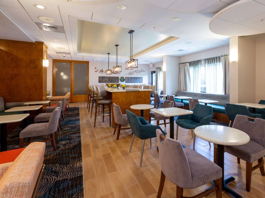 Un vestíbulo de hotel con varias zonas de estar, incluyendo cabinas y mesas, y un bar en el centro.