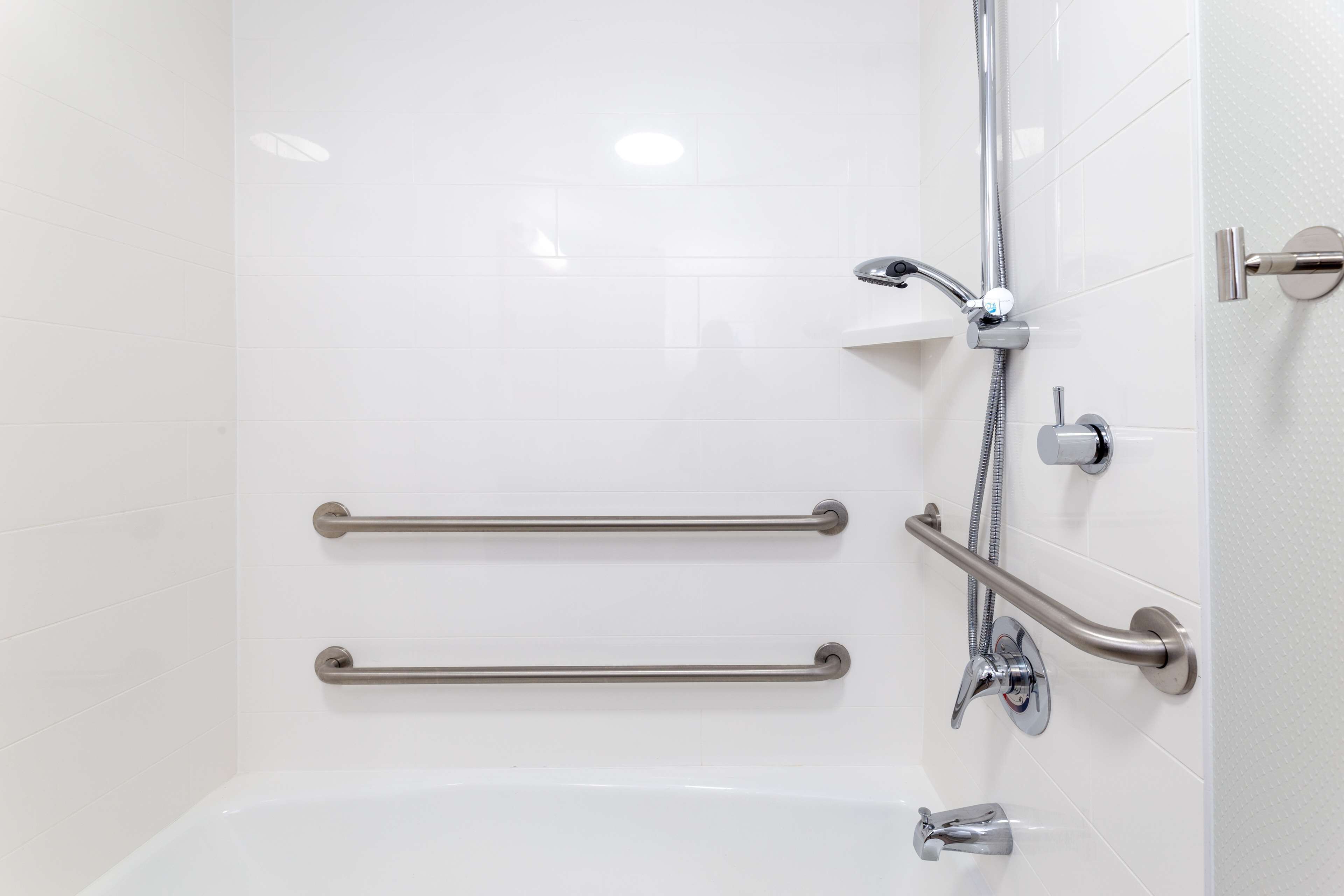 A bathroom with white tiled walls, a bathtub, and two grab bars installed for safety.