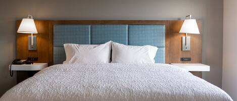 Una habitación de hotel con una cama grande, dos mesitas de noche con lámparas y un cabecero de madera.