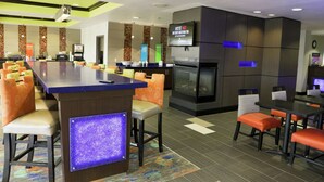 A modern hotel lobby with a bar area, seating, a television, and a fireplace.
