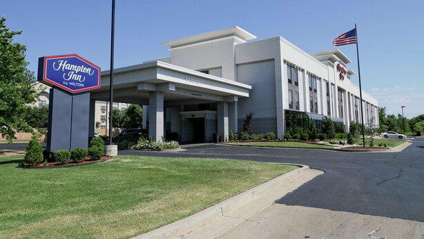 A Hampton Inn by Hilton building with a clear entrance, a flag, and a well-maintained lawn.