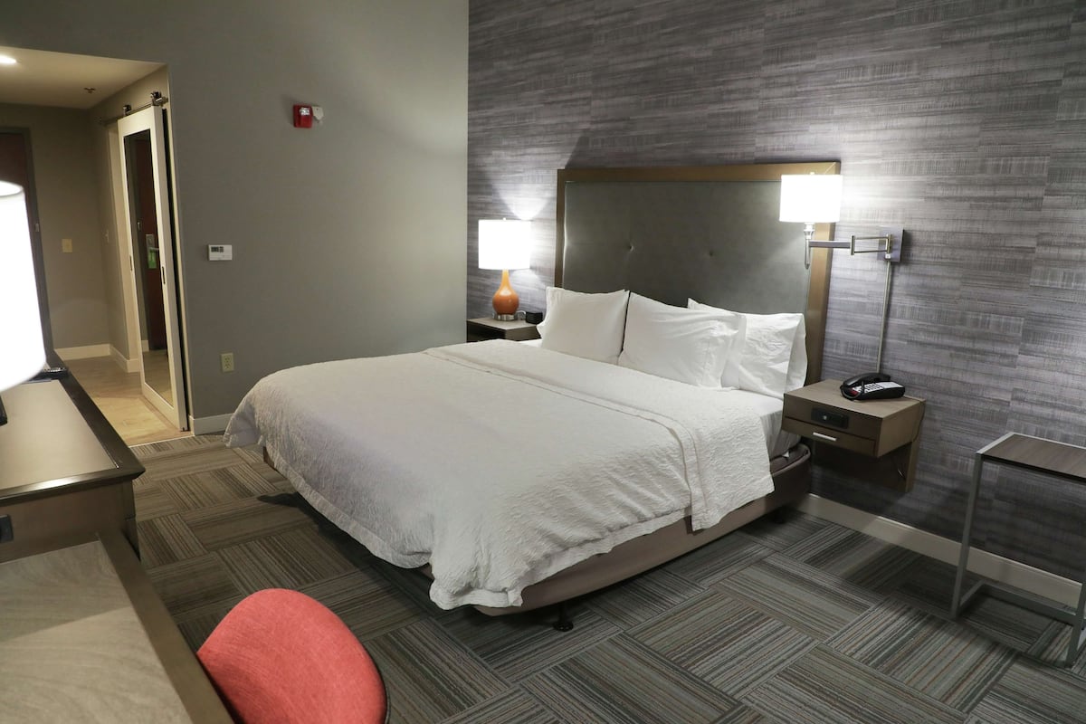 A hotel room with a large bed, a bedside table with a lamp, a nightstand, and a chair.