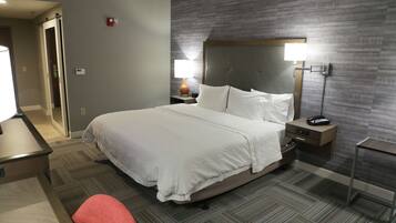 A hotel room with a large bed, a bedside table with a lamp, a nightstand, and a chair.
