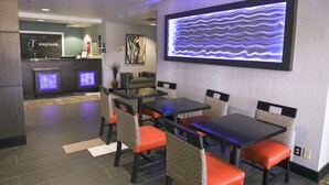 Un espace de restauration moderne avec des tables et des chaises, une cuisine en arrière-plan et une grande œuvre d’art lumineuse accrochée au mur.