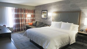 Une chambre d’hôtel avec un grand lit, un bureau, une chaise, un canapé et une table de chevet avec une lampe.