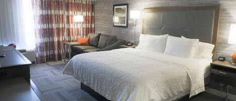 Habitación de hotel con una cama grande, un escritorio, una silla, un sofá y una mesita de noche con lámpara.