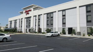 A modern hotel building with a prominent sign, multiple parking spaces, and a clear sky.