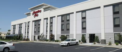 A modern hotel building with a prominent sign, multiple parking spaces, and a clear sky.