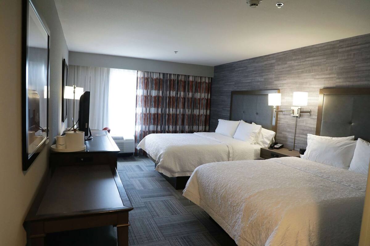 Una habitación de hotel con dos camas, un escritorio, un espejo y una ventana con cortinas.