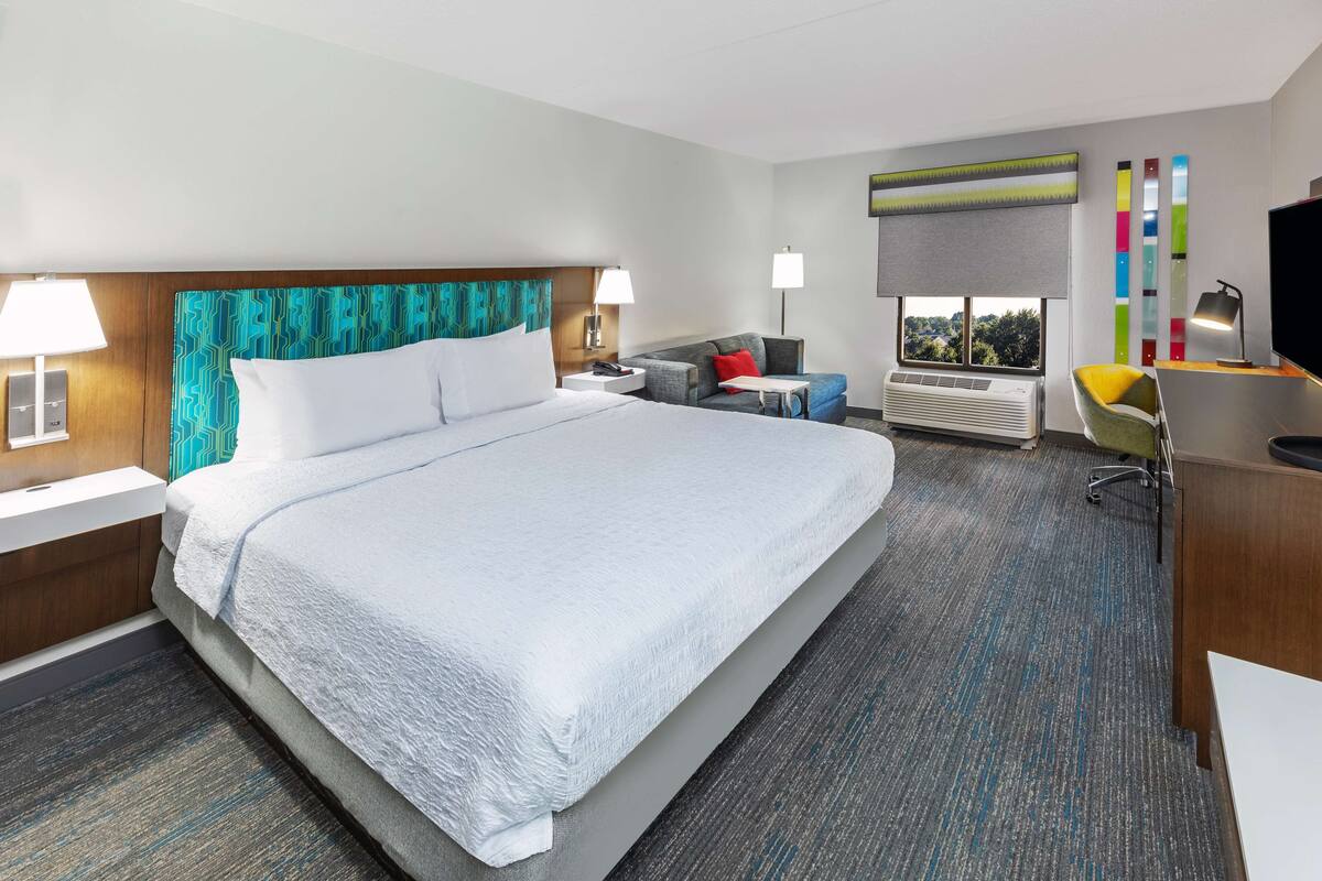 A hotel room with a large bed, a desk with a chair, a TV, and a window with a view.